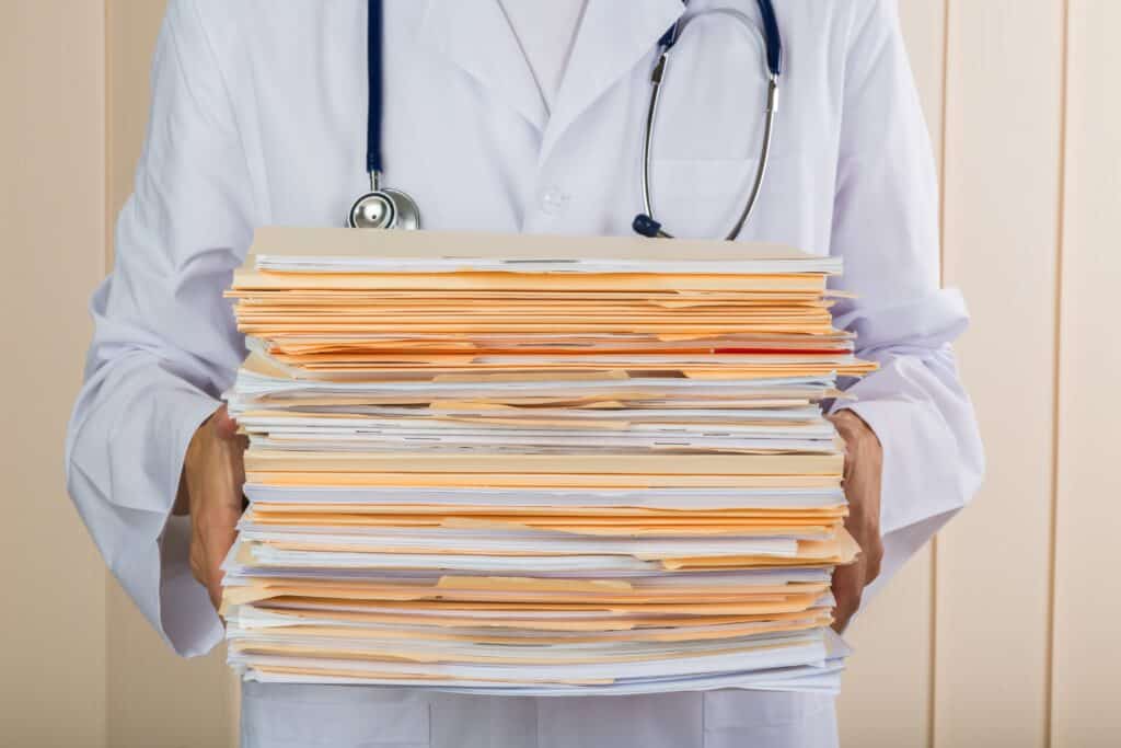 close up of a doctor with stacks of medical folders and files and a stethoscope